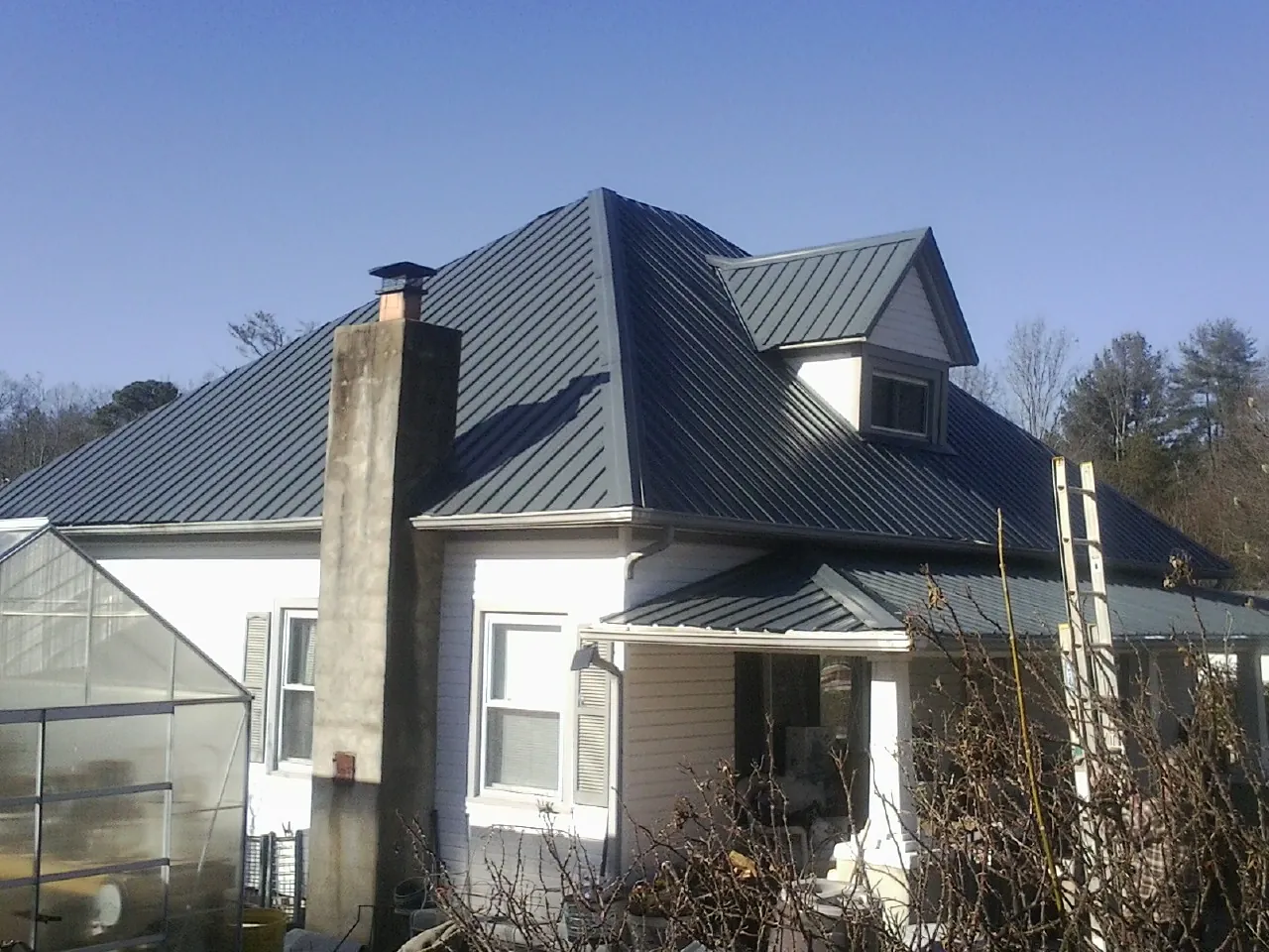 Dark blue standing seam metal roof on a white farmhouse with dormer — Slate & Tile Roof Repair by Roofing Brothers in Brookline