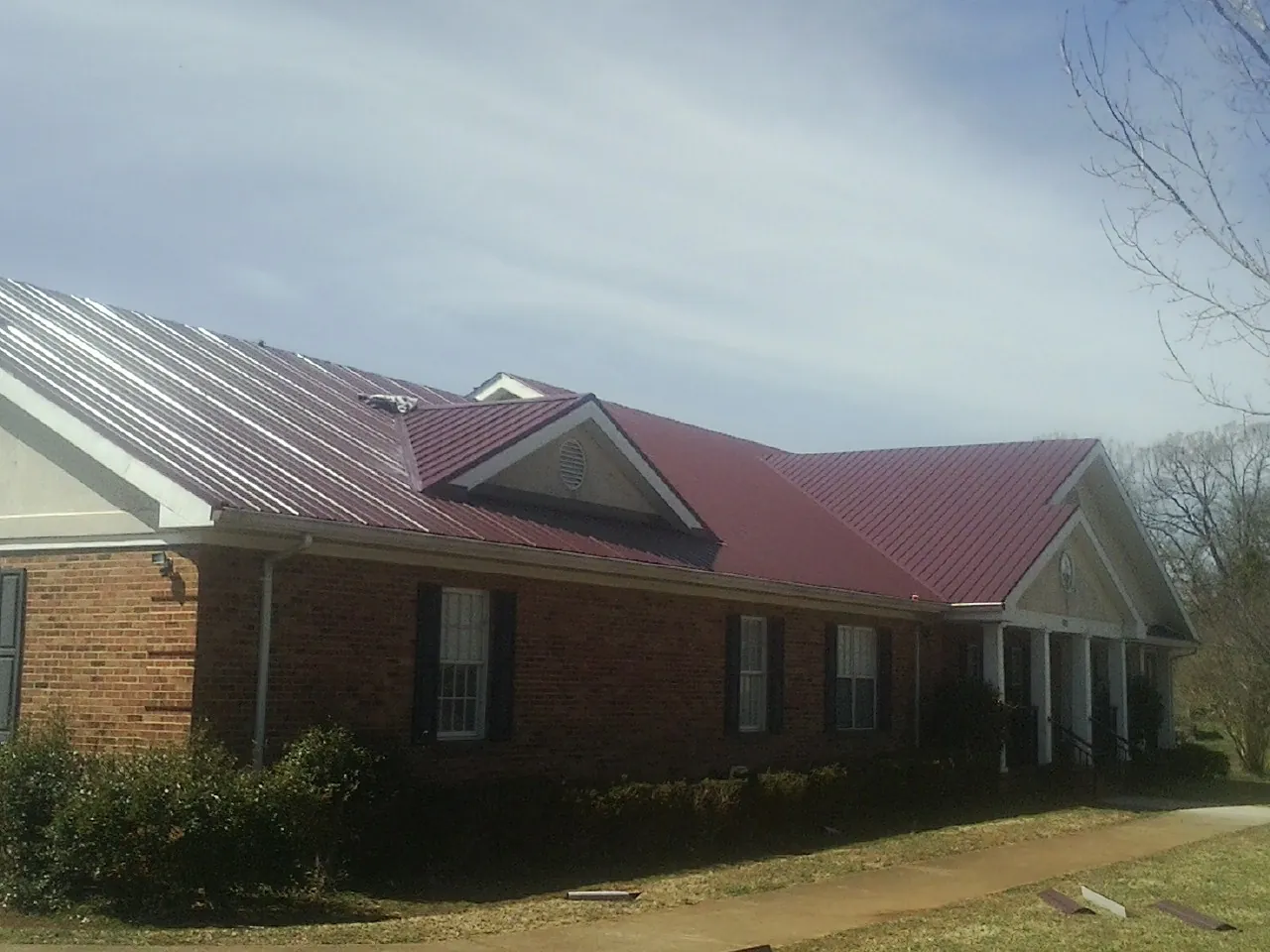 Red metal roof with gabled entries on a long brick building, from a Hail Damage Roof Repair job in Brookline